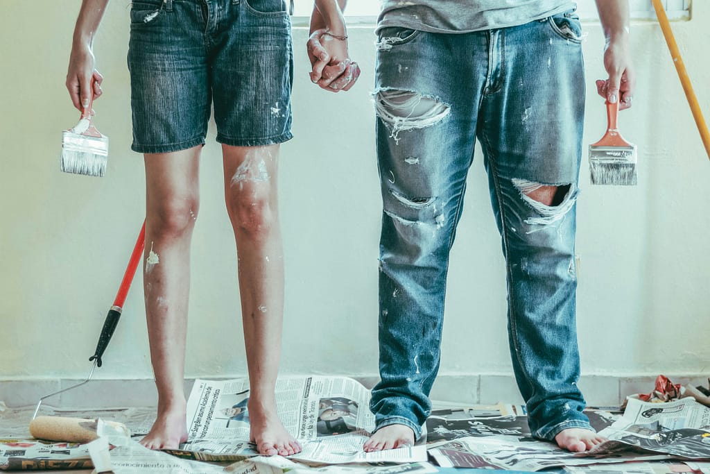 Couple midway through a property renovation, dressed in work clothes covered in paint and plaster.